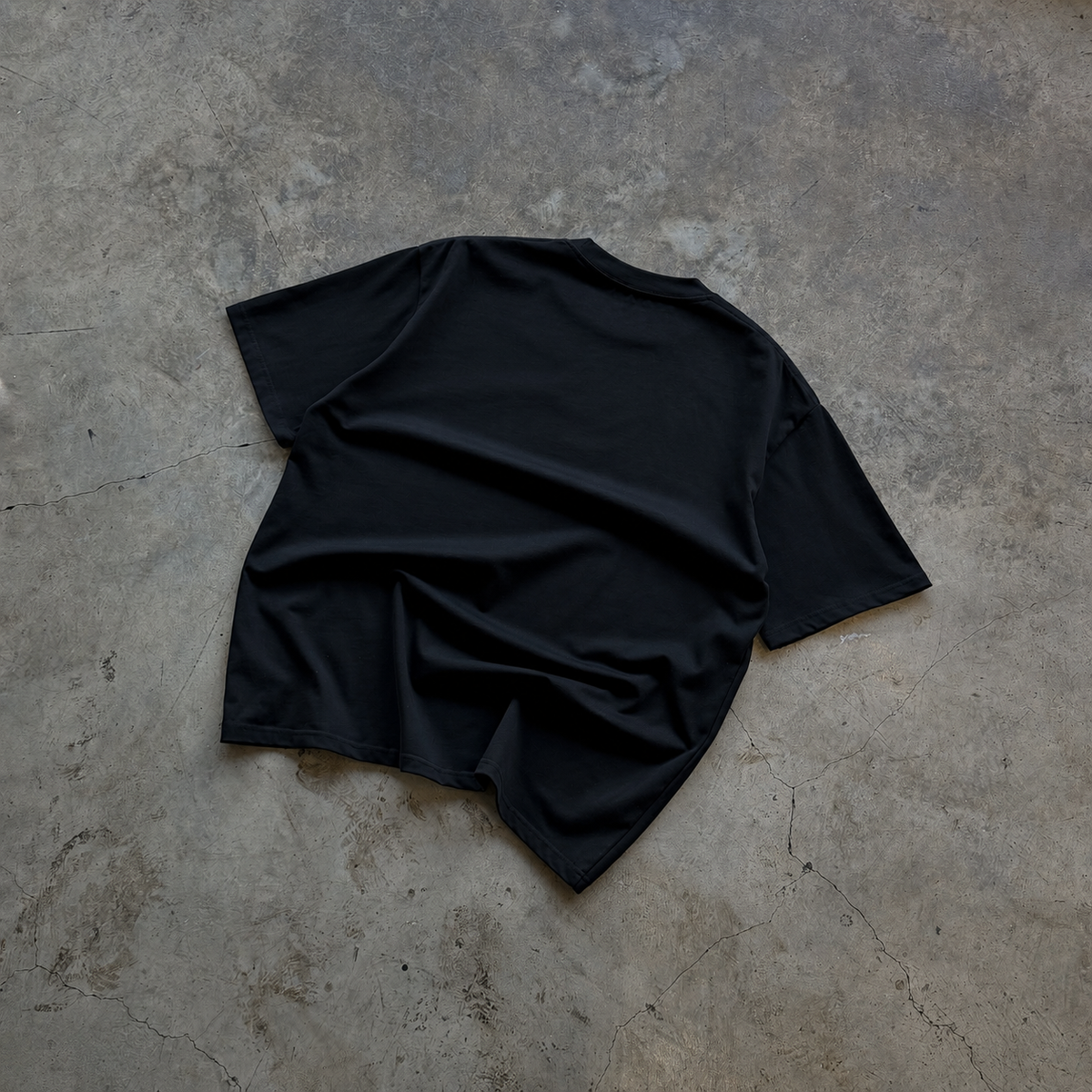 A black t-shirt laid flat on a textured gray concrete floor.